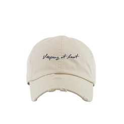 Beige cap with 'sleeping at last' embroidery on a white background