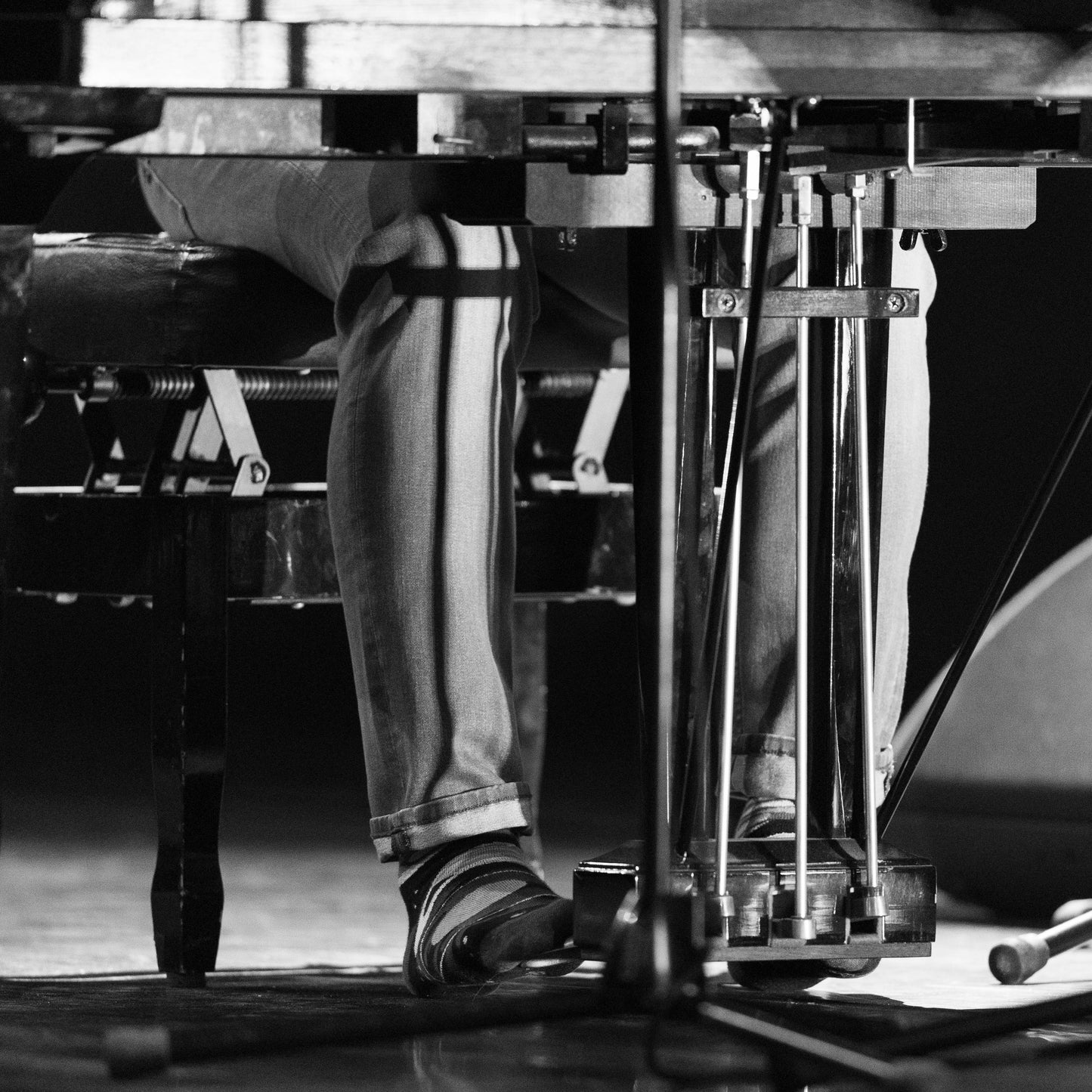 Close-up of a piano with a person's legs and feet visible, wearing pants and space socks.